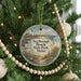A round ornament hanging on a Christmas tree, featuring a lighthouse and a beach scene.