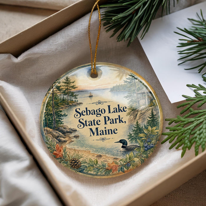 A decorative ornament with a scenic landscape of Sebago Lake State Park, Maine, featuring pine trees, a lake, and a bird.