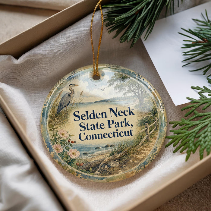 A decorative ornament with the text "Selden Neck State Park, Connecticut" on it, hanging from a string. The ornament is placed in a box with pine branches and a white paper.