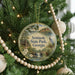 A round ornament hanging on a Christmas tree, featuring a scenic image of a lake, trees, and a bird.