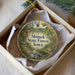 A decorative ornament in a box, featuring a scenic landscape with a river, trees, and wildlife.