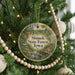 A round ornament hanging on a Christmas tree, featuring a scenic landscape with a stream and a bridge.