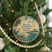 A round ornament hanging on a Christmas tree, featuring a serene scene of a pier and palm trees against a sunset backdrop.