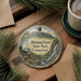 A decorative ornament featuring a scenic landscape with a waterfall and mountains, hanging on a wooden surface.