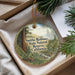 A round ornament with a forest scene and text, placed in a box with pine branches.