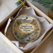 A decorative ornament in a box, featuring a scenic landscape with mountains, a river, and desert vegetation.