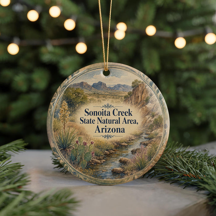 A circular ornament with a scenic landscape of Sonoita Creek, the Sonoita Creek State Natural Area in Arizona, displayed on a table with pine branches and twinkling lights in the background.