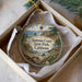 A decorative ornament in a box, featuring a scenic landscape with a lighthouse and a deer in the foreground, surrounded by greenery.