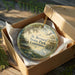 A circular ornament in a wooden box, featuring a scenic image of St. Bernard State Park in Louisiana.