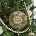 A round ornament hanging on a Christmas tree, featuring a scenic landscape with mountains, a river, and a bridge.