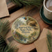 A round ornament with a scenic image of Starved Rock State Park, Illinois, hanging on a wooden surface.