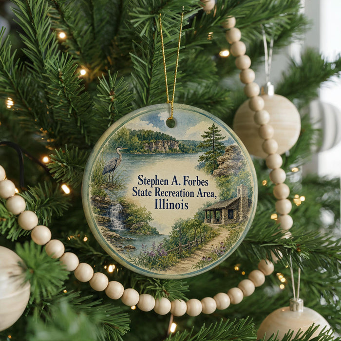A round ornament hanging on a Christmas tree, featuring a scenic landscape with a lake, mountains, and a bird.