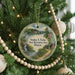 A round ornament hanging on a Christmas tree, featuring a scenic landscape with a lake, mountains, and a bird.
