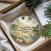 A decorative ornament with a beach scene and a bird, placed in a box with pine branches.
