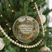 A round ornament hanging on a Christmas tree, featuring a scenic landscape with mountains, trees, and a stream.