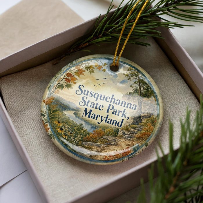 A decorative ornament in a box, featuring a scenic landscape with trees, mountains, and a river.