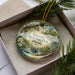 A decorative ornament in a box, featuring a scenic image of Suwannee River State Park in Florida.