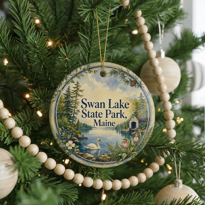 A round ornament hanging on a Christmas tree, featuring a scenic image of Swan Lake State Park in Maine.