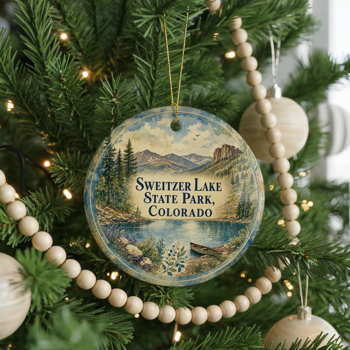 A round ornament hanging on a Christmas tree, featuring a scenic landscape with mountains and a lake.
