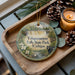 A decorative ornament featuring a scenic image of Tahquamenon Falls State Park, Michigan, with pine cones and a candle on a wooden tray.
