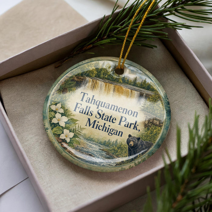 A decorative ornament featuring a scenic image of Tahquamenon Falls State Park, Michigan, with a black bear in the foreground.