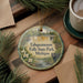 A decorative ornament featuring a waterfall and pine trees, with the text "Tahquamenon Falls State Park, Michigan" printed on it. The ornament is placed on a wooden surface, surrounded by pine branches and a cup of coffee.