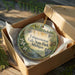 A round ornament in a brown box, featuring a scenic image of Tahquamenon Falls State Park, Michigan.