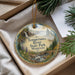 A decorative ornament with a scenic landscape of a river, forest, and waterfall, hanging from a string.