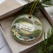 A decorative ornament in a box, featuring a scenic landscape with a river, bridge, and trees, along with the text "Tishomingo State Park, Mississippi".