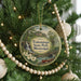 A round ornament hanging on a Christmas tree, featuring a scenic landscape with a waterfall and a bridge.