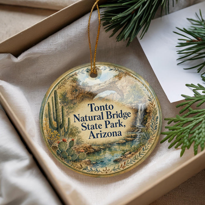 A decorative ornament with a natural bridge and desert landscape, placed in a box with pine branches.
