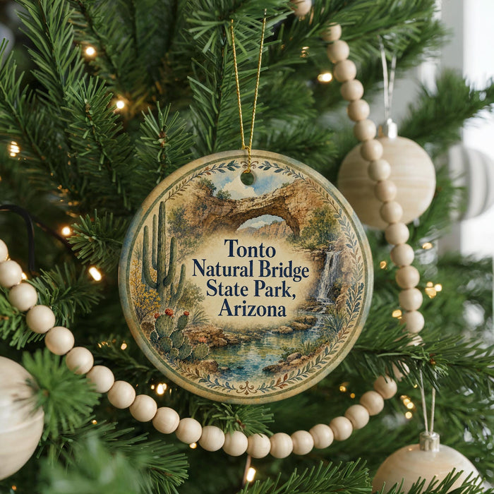 A round ornament hanging on a Christmas tree, featuring a desert landscape with a bridge and cacti.