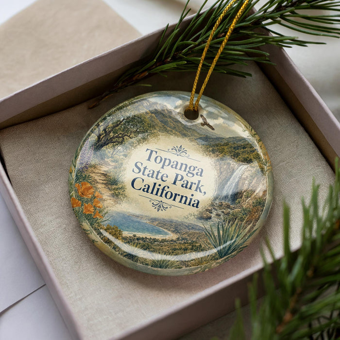 A decorative ornament in a box, featuring a scenic landscape with mountains, trees, and water.