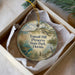A round ornament with a scenic landscape of a beach, grass, and a bird, hanging from a string.