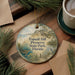A round ornament with a scenic landscape of a beach, pine trees, and a bird, hanging on a wooden surface.