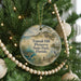 A round ornament hanging on a Christmas tree, featuring a scenic landscape with a beach, palm trees, and a bird.
