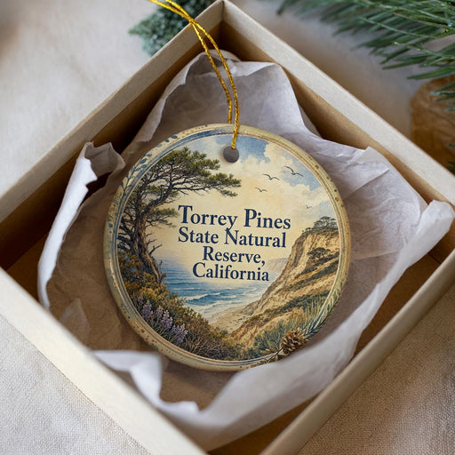 A decorative ornament in a box, featuring a scenic landscape with a pine tree, mountains, and a body of water.