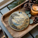 A wooden tray with a decorative ornament featuring a scenic landscape of Torrey Pines State Natural Reserve, California, and pine cones.