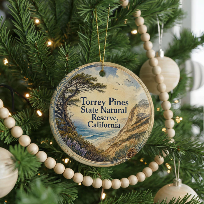 A round ornament hanging on a Christmas tree, featuring a scenic landscape with a pine tree, mountains, and a body of water.