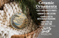 Ceramic ornaments, featuring a round ornament with a landscape design, are displayed in a basket with pine branches.