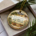 A decorative ornament with a picture of Tubac State Historic Park, Arizona, displayed in a box with pine branches.