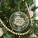 A round ornament hanging on a Christmas tree, featuring a scenic landscape with a lake, waterfall, and houses.