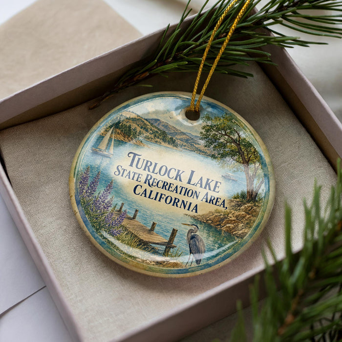 A decorative ornament in a box, featuring a scenic landscape with a lake, mountains, and a bird.