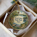 A decorative ornament in a box, featuring a scenic landscape with a lake, cabin, and trees.