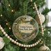 A round ornament hanging on a Christmas tree, featuring a scenic landscape with a castle, trees, and a river.