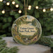 A round ornament with a scenic landscape of Union Grove State Park, Iowa, featuring a lighthouse, a river, and trees, is displayed against a blurred background of Christmas lights.