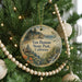 A round ornament hanging on a Christmas tree, featuring a scenic landscape with a house, trees, and a body of water.