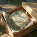 A decorative ornament in a box, featuring a scenic landscape with a house and trees, with the text "Van Damme State Park, California" printed on it.