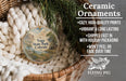 Ceramic ornaments, featuring a round wooden ornament with a landscape scene and text, are displayed in a basket with greenery.