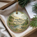 A decorative ornament with a scenic landscape of a river, mountains, and greenery, hanging from a string.